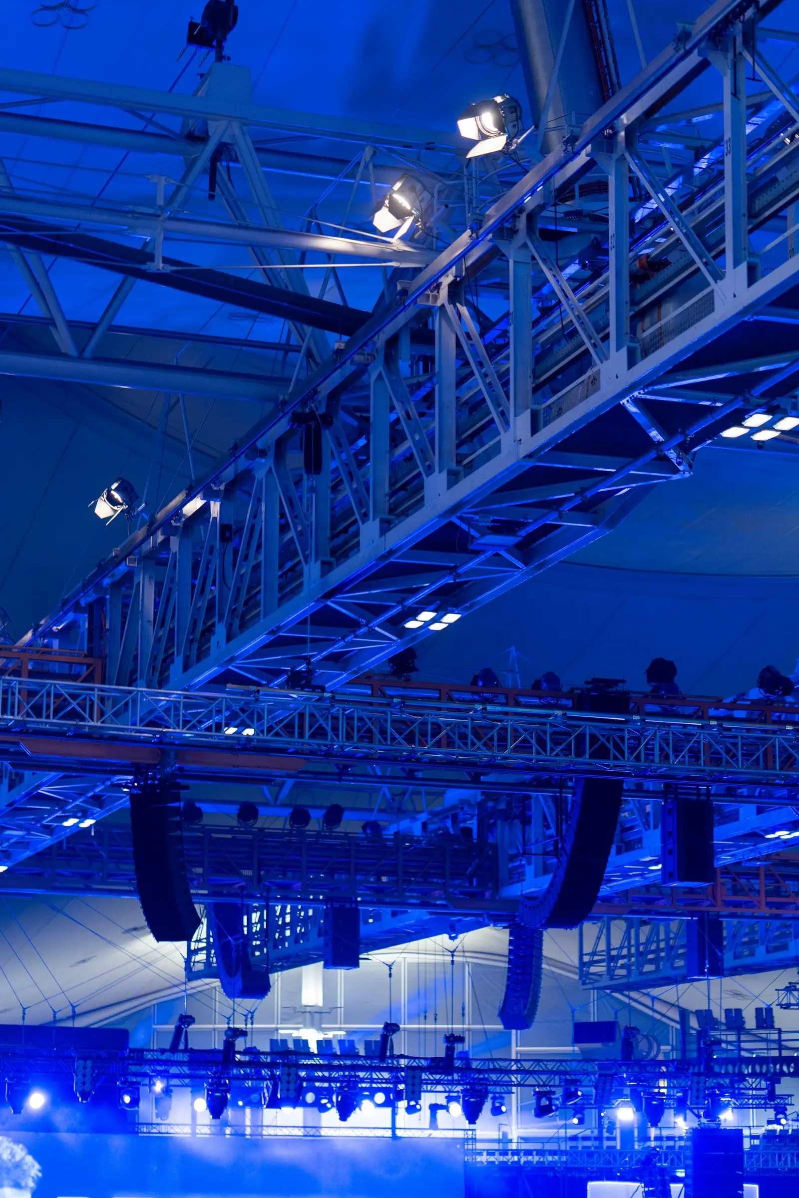 Régie événementielle : ponts d’éclairage, projecteurs et systèmes de son d’une grande salle baignée de lumière bleue.